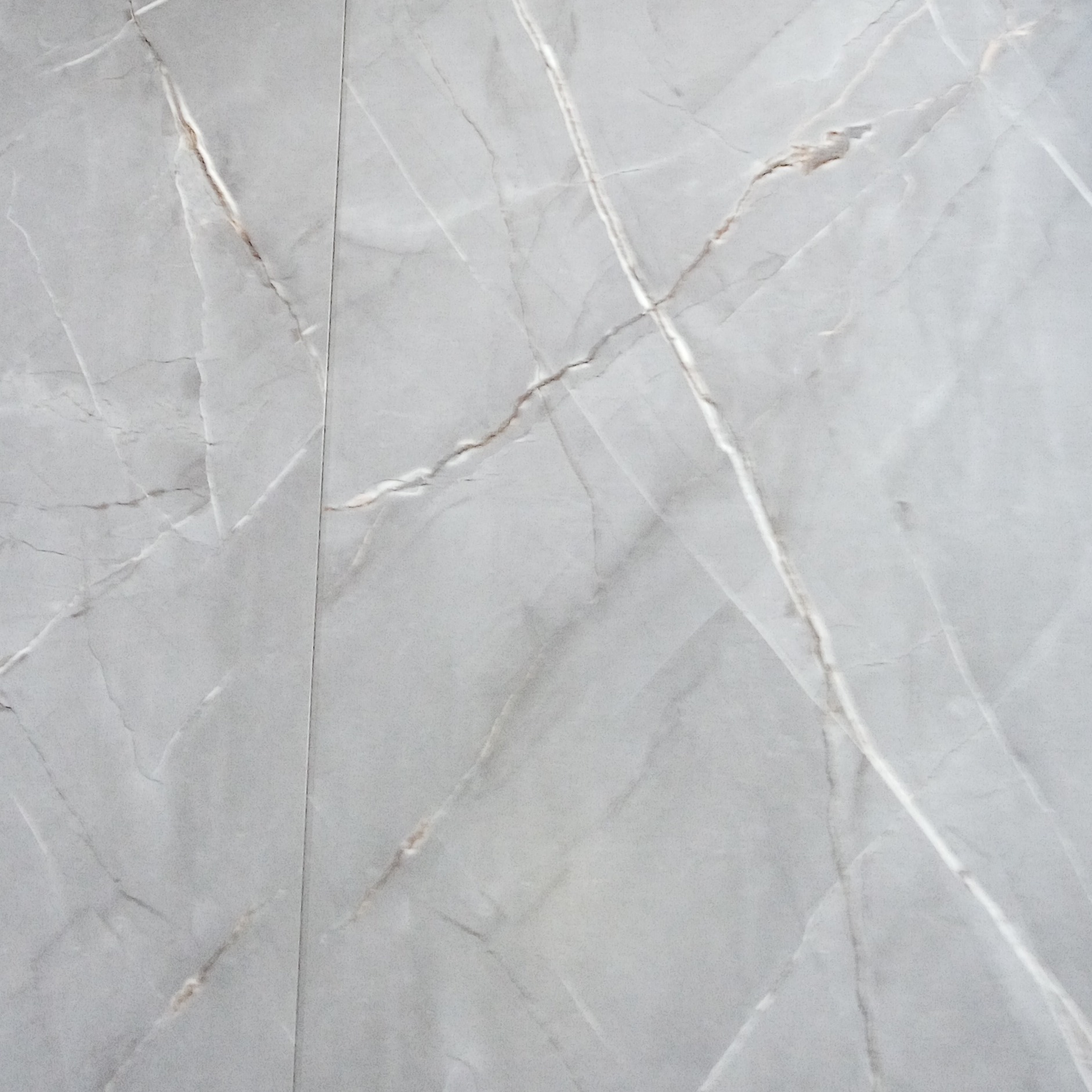 Powiększony widok szarej, matowej płytki imitującej marmur z wyraźnymi, jasnymi żyłami. Płytki ułożone pionowo, widoczne łączenie między nimi.