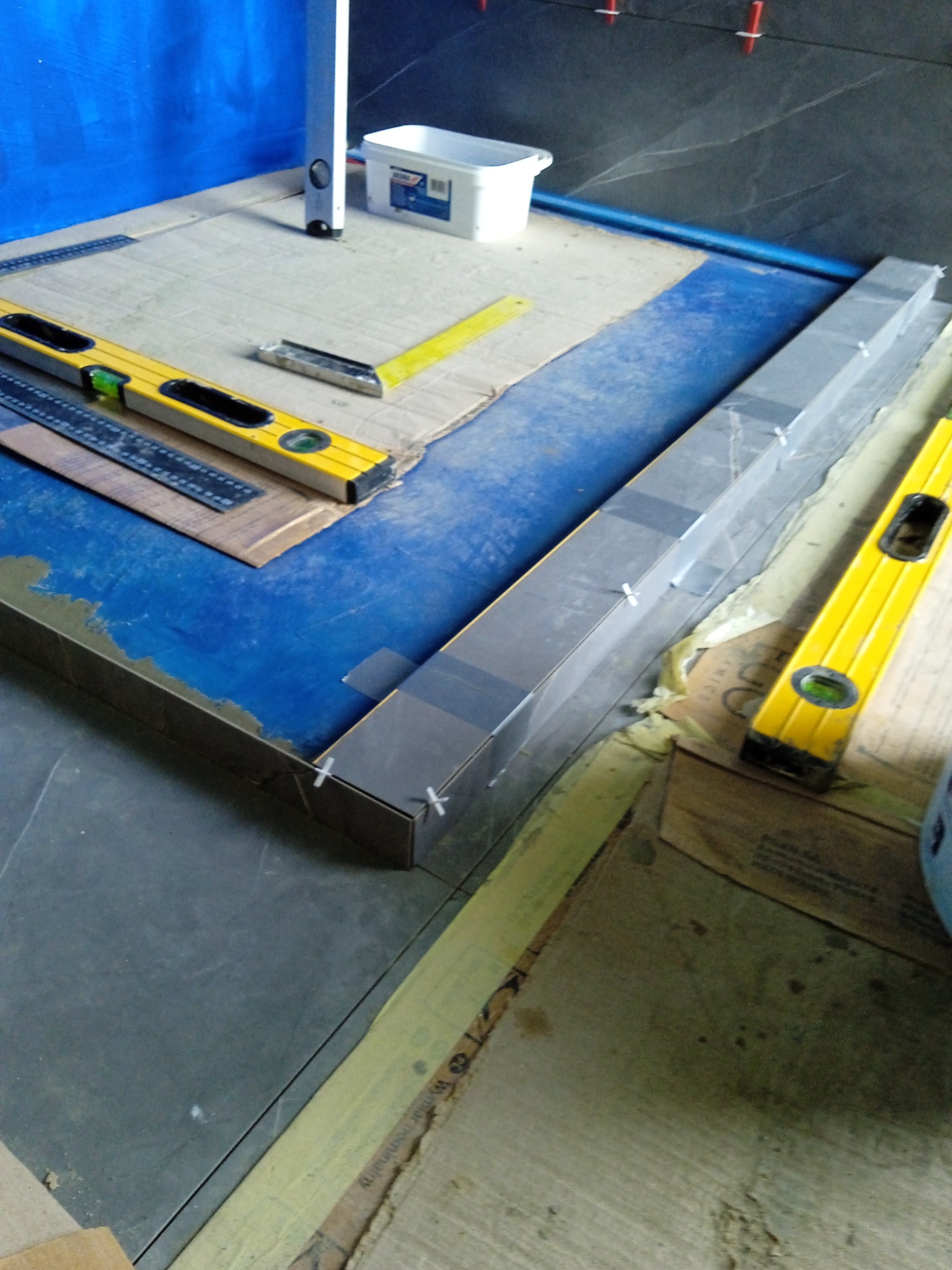 Montaż płytek podłogowych w łazience, widoczne poziomice, listwy, krzyżyki dystansowe i narzędzia, przygotowanie do fugowania.