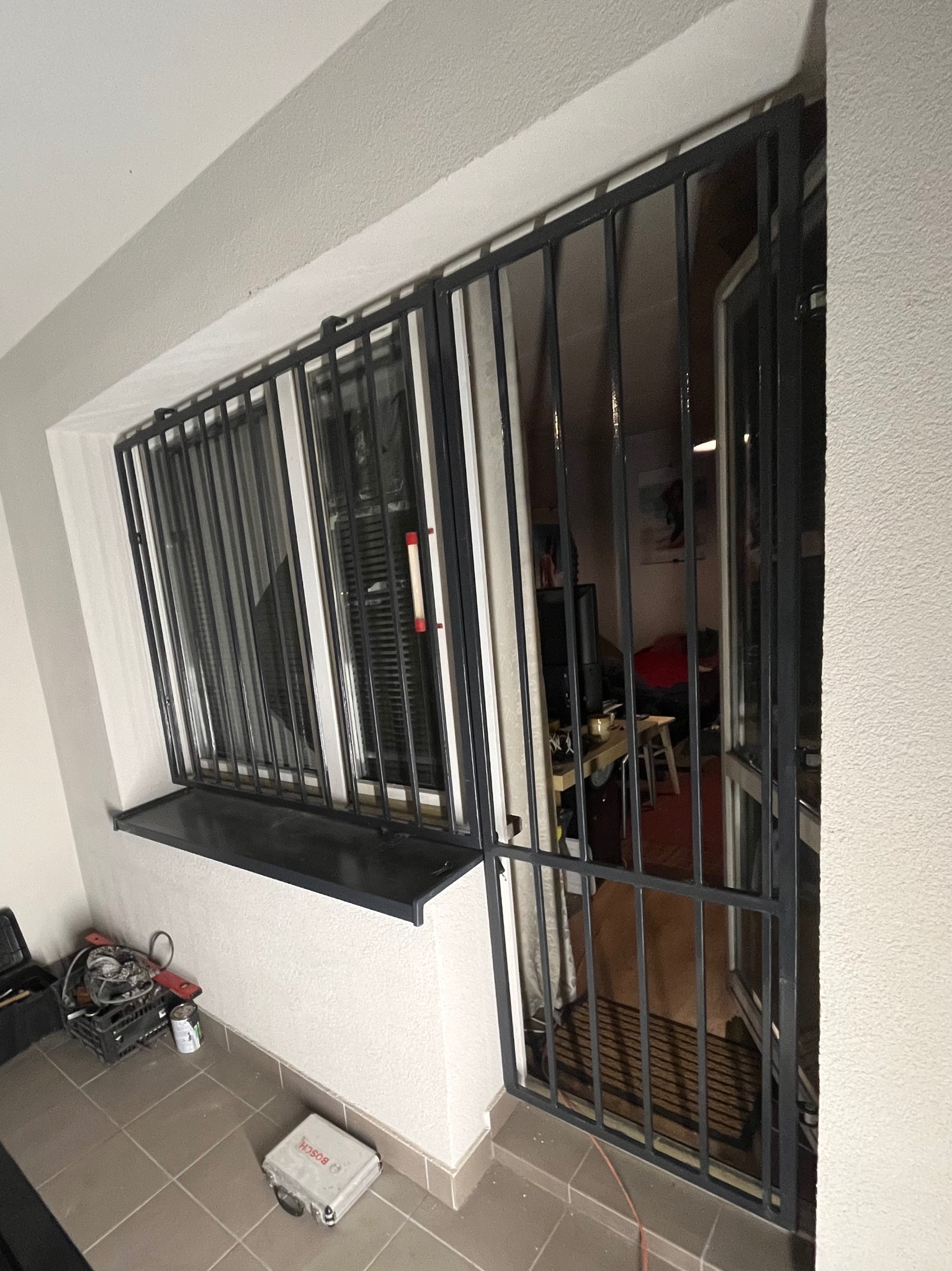 Metalowa krata okienna i drzwiowa, zabezpieczenie antywłamaniowe, widoczne narzędzia montera w tle.