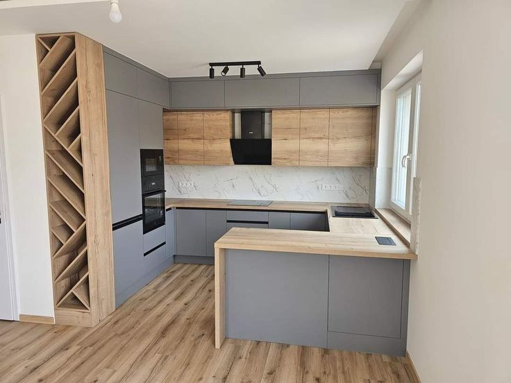 Nowoczesna kuchnia w szarościach i drewnie: zabudowa z półwyspem, marmurowy backsplash, oświetlenie punktowe i regał na wino. Jasne drewno na podłodze.