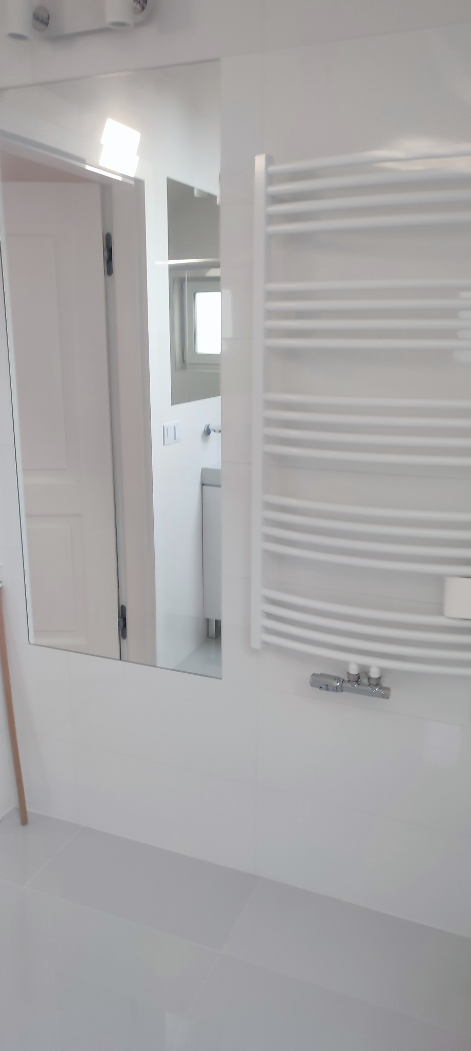 Minimalistyczna, biała łazienka w Gliwicach z grzejnikiem drabinkowym i lustrem odbijającym fragment wnętrza.