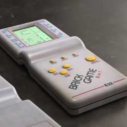 CRE8VISION - Retro przenośna konsola Brick Game 8 in 1 z wyświetlaczem pokazującym grę w Tetris, leżąca na szarym tle.