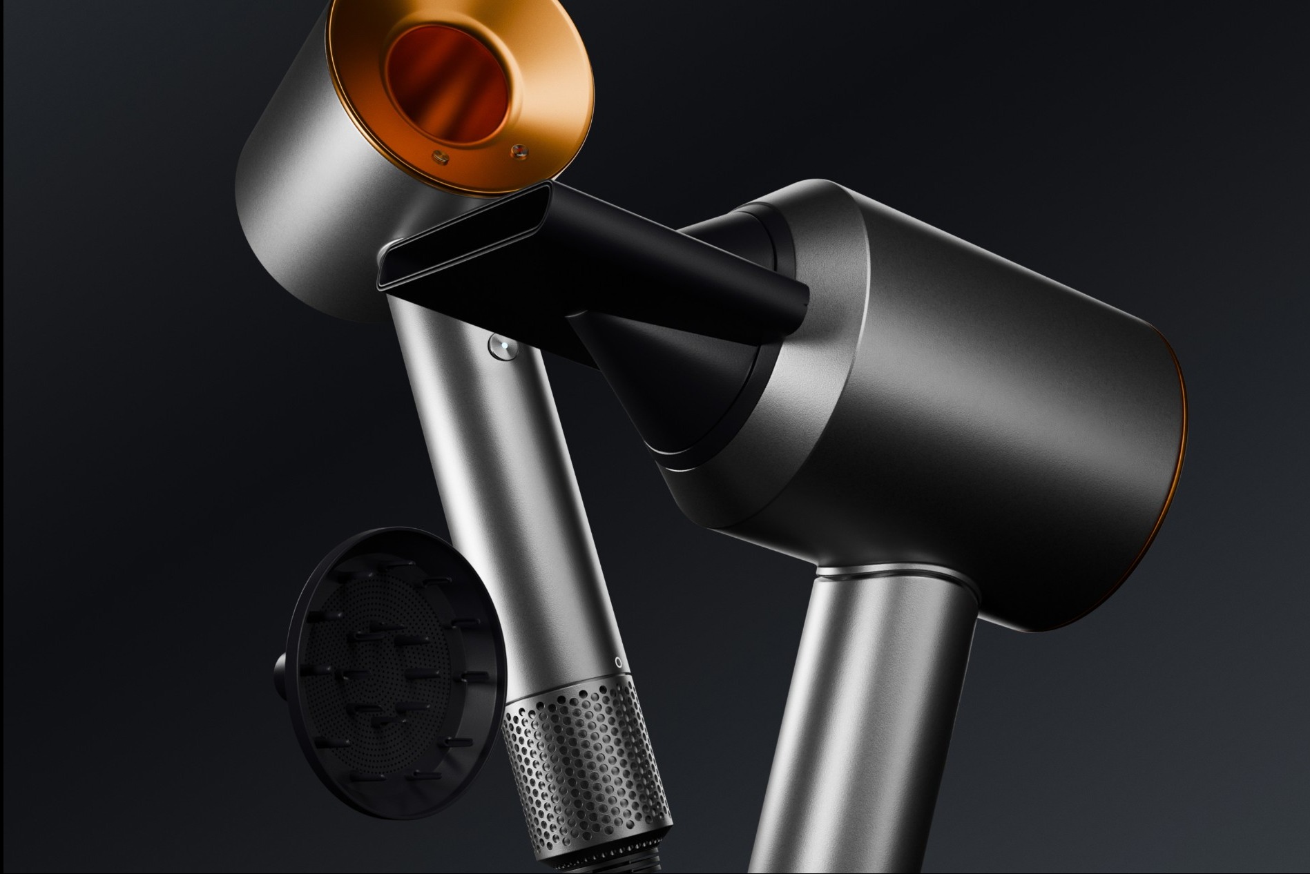 Dwa nowoczesne suszarki do włosów w kolorze srebrnym i czarnym z miedzianymi akcentami, widoczne z dyfuzorem, na ciemnoszarym tle.