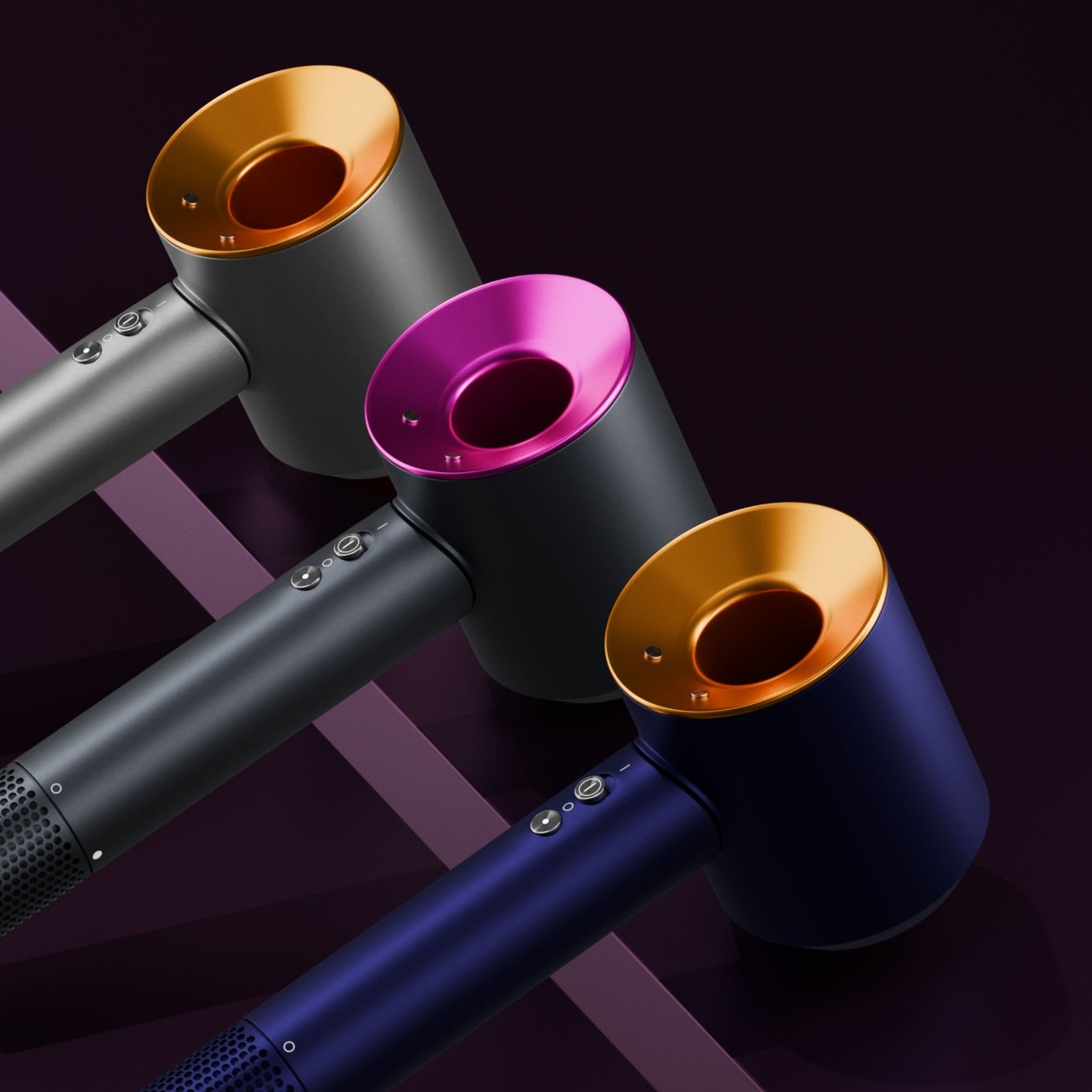 Trzy nowoczesne suszarki do włosów w kolorach: szarym ze złotym akcentem, czarnym z różowym i granatowym ze złotym, ułożone ukośnie na ciemnym tle z geometrycznym wzorem.