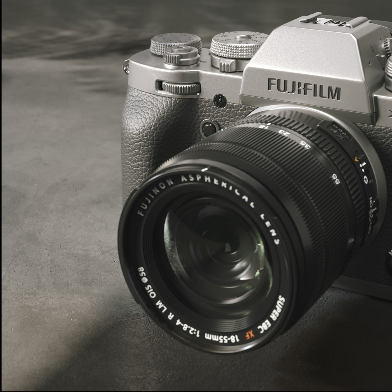 Srebrny aparat Fujifilm z obiektywem Fujinon 18-55mm na ciemnym, teksturowanym tle, z widocznymi detalami obiektywu i korpusu.