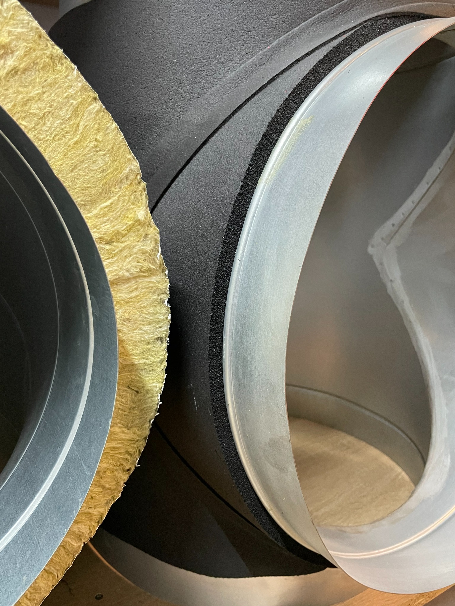 Przekrój przez izolowane kanały wentylacyjne: wełna mineralna, pianka izolacyjna i metalowy przewód.