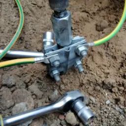 Złącze uziemiające z przewodem ochronnym żółto-zielonym, klucz nasadowy obok, w wykopie ziemnym.