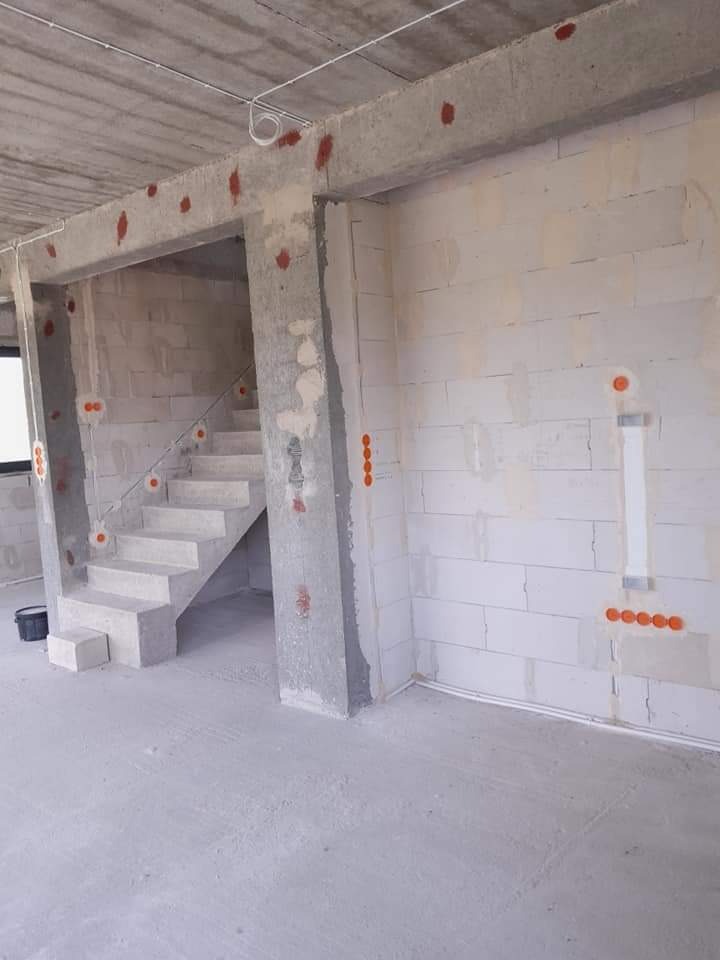 Surowy stan wnętrza z widoczną instalacją elektryczną: kable prowadzone po suficie, puszki elektryczne w ścianach z betonu komórkowego, betonowe schody w tle.