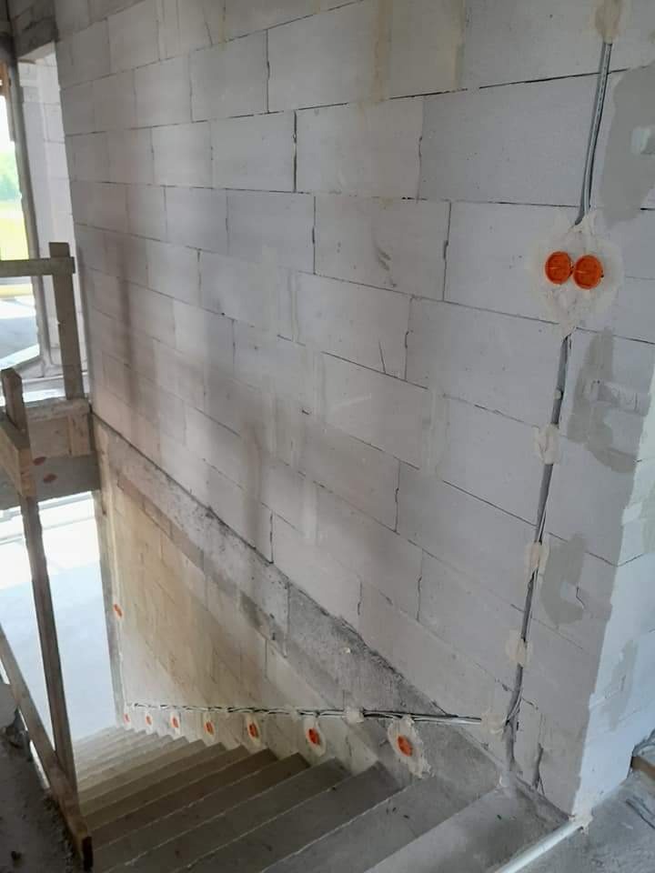 Wewnętrzne ściany z betonu komórkowego w trakcie budowy, widoczne puszki elektryczne i przewody prowadzone po ścianie w peszlu, schody w surowym stanie.