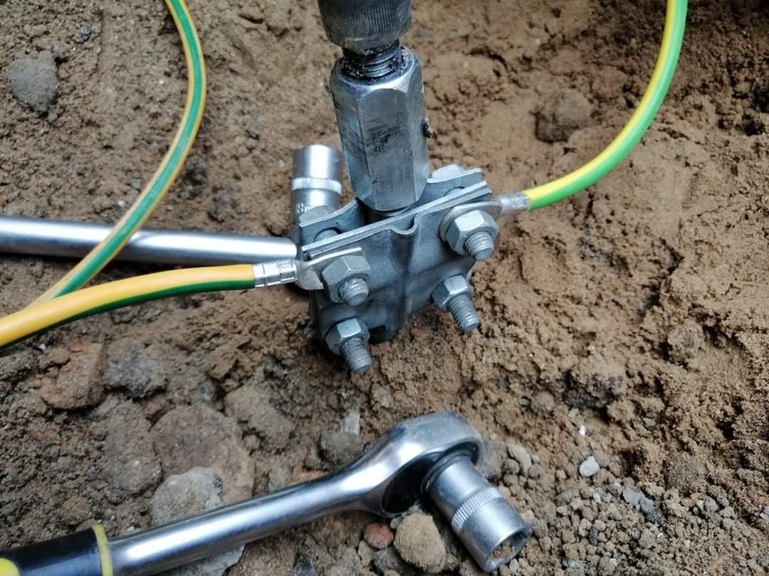 Złącze uziemiające z przewodem ochronnym żółto-zielonym, klucz nasadowy obok, w wykopie ziemnym.