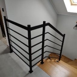 Mikołaj Jeliński Deerspaw - Nowoczesna, czarna balustrada schodowa z poziomymi prętami, zamontowana przy drewnianych schodach w jasnym wnętrzu z oknem dachowym i designerską lampą na ścianie.