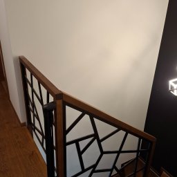 Mikołaj Jeliński Deerspaw - Drewniane schody z nowoczesną balustradą o geometrycznym wzorze, czarne elementy konstrukcyjne, drewniana poręcz, widok z góry.