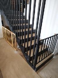 Czarne, metalowe schody z drewnianymi stopniami i zabezpieczeniem dla dziecka na dole, widok z dołu, jasne wnętrze.