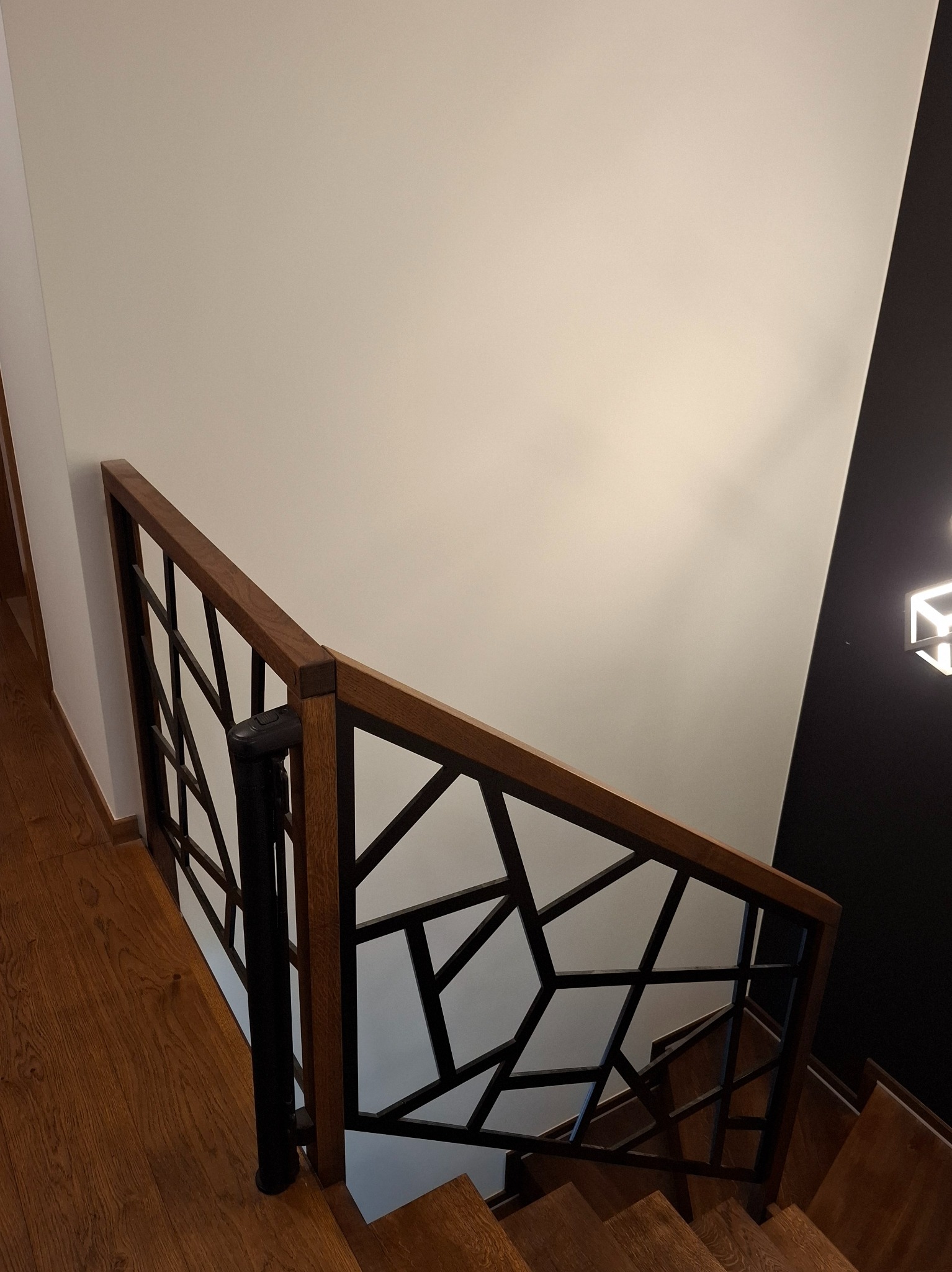 Drewniane schody z nowoczesną balustradą o geometrycznym wzorze, czarne elementy konstrukcyjne, drewniana poręcz, widok z góry.