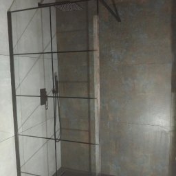 Lukasz Stadnik - Nowoczesna kabina prysznicowa z czarnymi profilami i deszczownicą, szare płytki na ścianach i podłodze, minimalistyczny design.