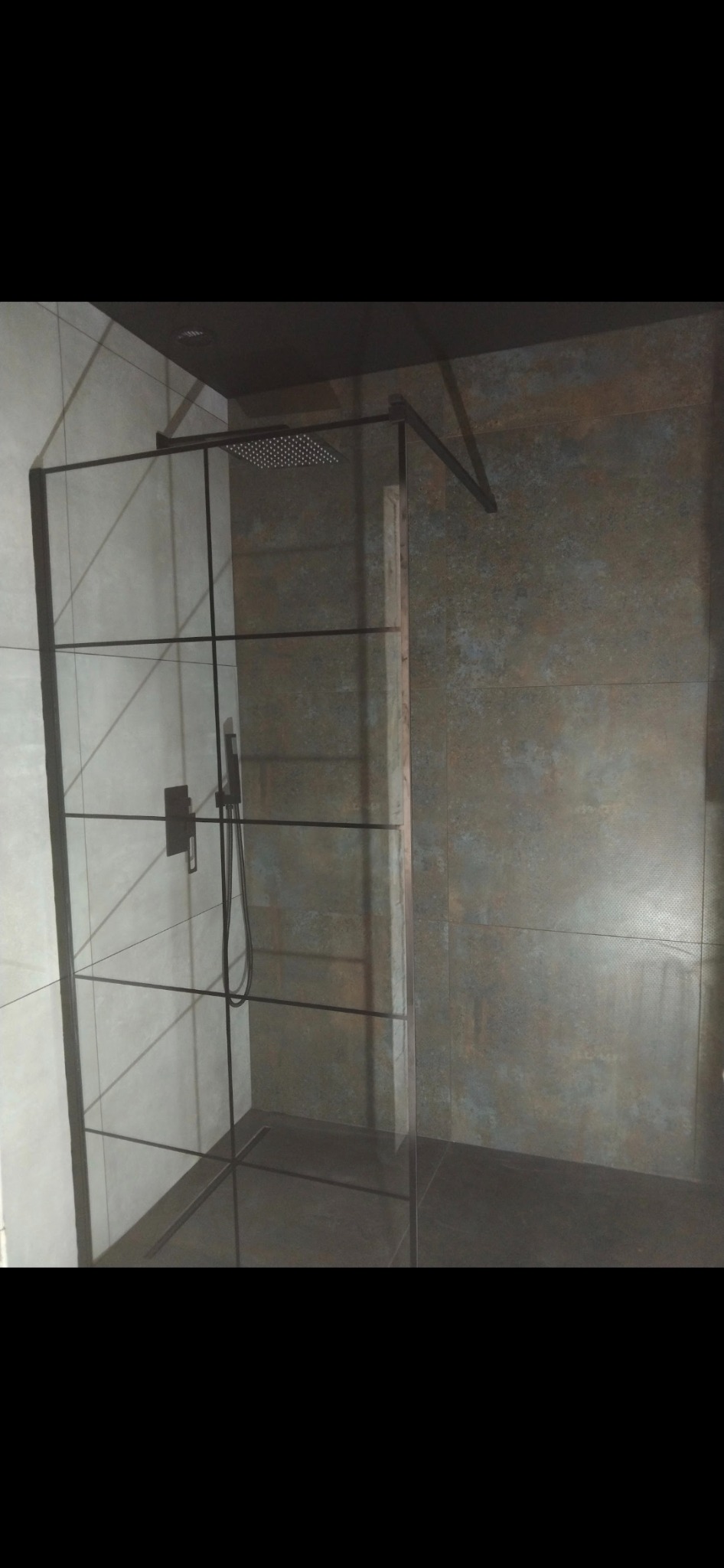 Nowoczesna kabina prysznicowa z czarnymi profilami i deszczownicą, szare płytki na ścianach i podłodze, minimalistyczny design.