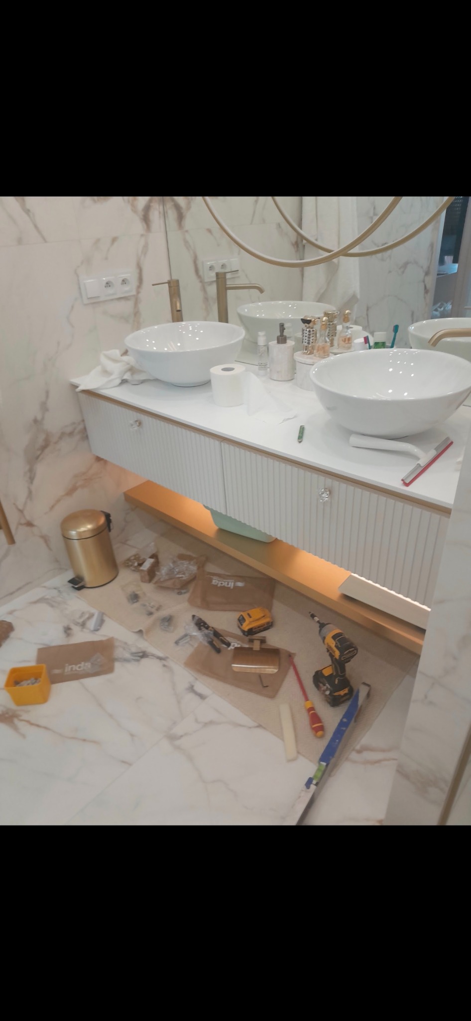 Montaż szafki umywalkowej w łazience z marmurowymi płytkami; widoczne narzędzia, elementy montażowe i umywalki nablatowe.