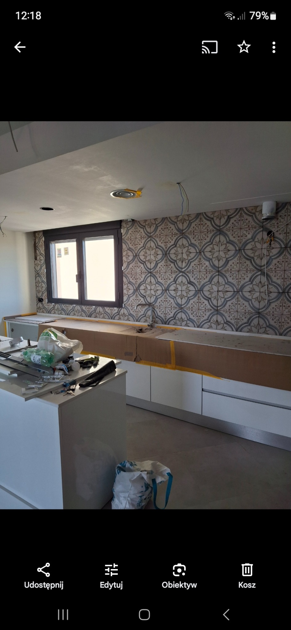 Montaż płytek ściennych z wzorem geometrycznym w kuchni, zabezpieczone blaty robocze, widoczne narzędzia i materiały budowlane, surowy stan wykończenia.