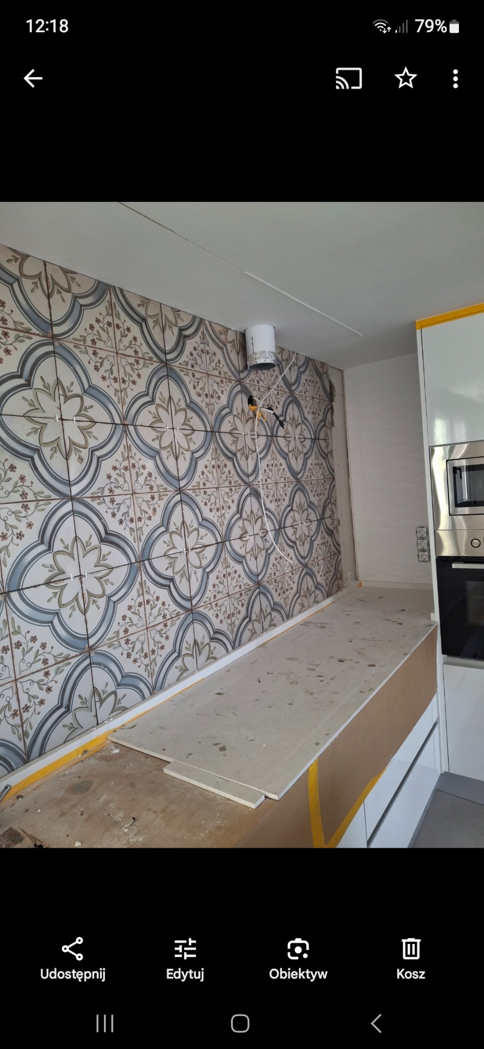 Montaż płytek dekoracyjnych na ścianie kuchni, widoczne krzyżyki dystansowe, fragment zabudowy kuchennej i przygotowany blat pod zabudowę.