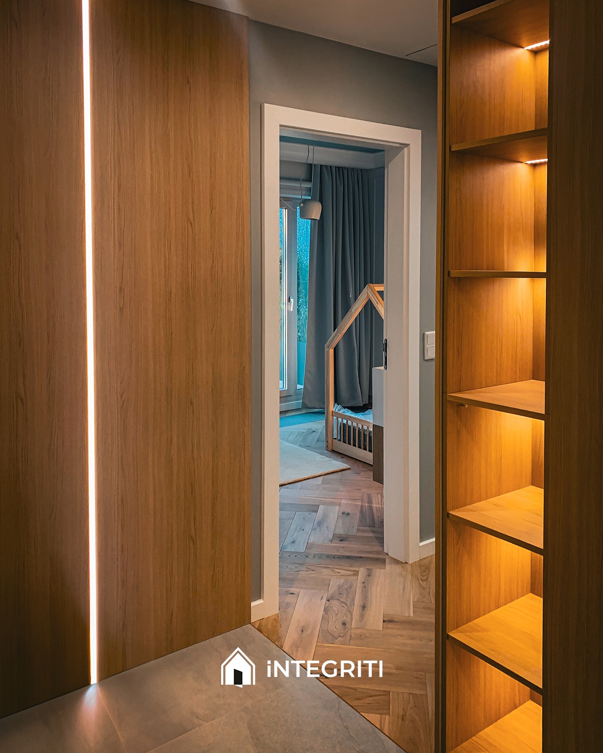 Nowoczesne wnętrze z drewnianą zabudową, podświetlaną pionową listwą LED, widok na pokój dziecięcy z łóżkiem w kształcie domku, parkiet ułożony w jodełkę.