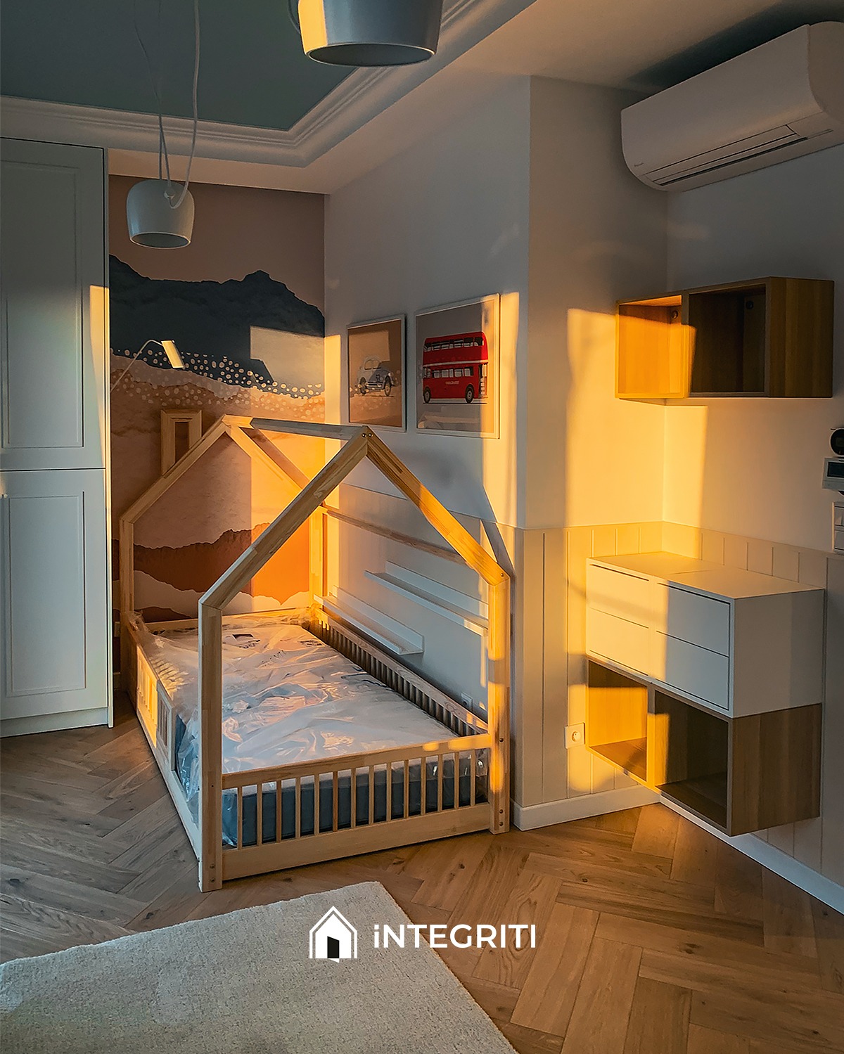 Pokój dziecięcy z drewnianym łóżkiem w kształcie domku, panelami ściennymi i minimalistycznymi szafkami wiszącymi, oświetlony ciepłym, zachodzącym słońcem wpadającym przez okno.