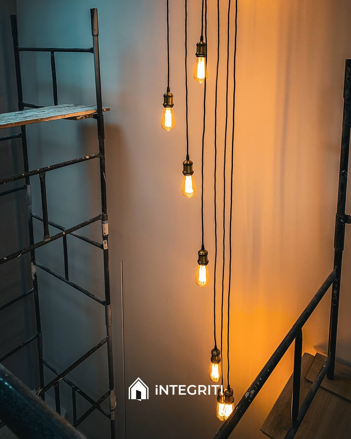 Wiszące żarówki Edisona na czarnych kablach, widoczne rusztowanie i balustrada, ciepłe światło podkreśla industrialny charakter wnętrza.