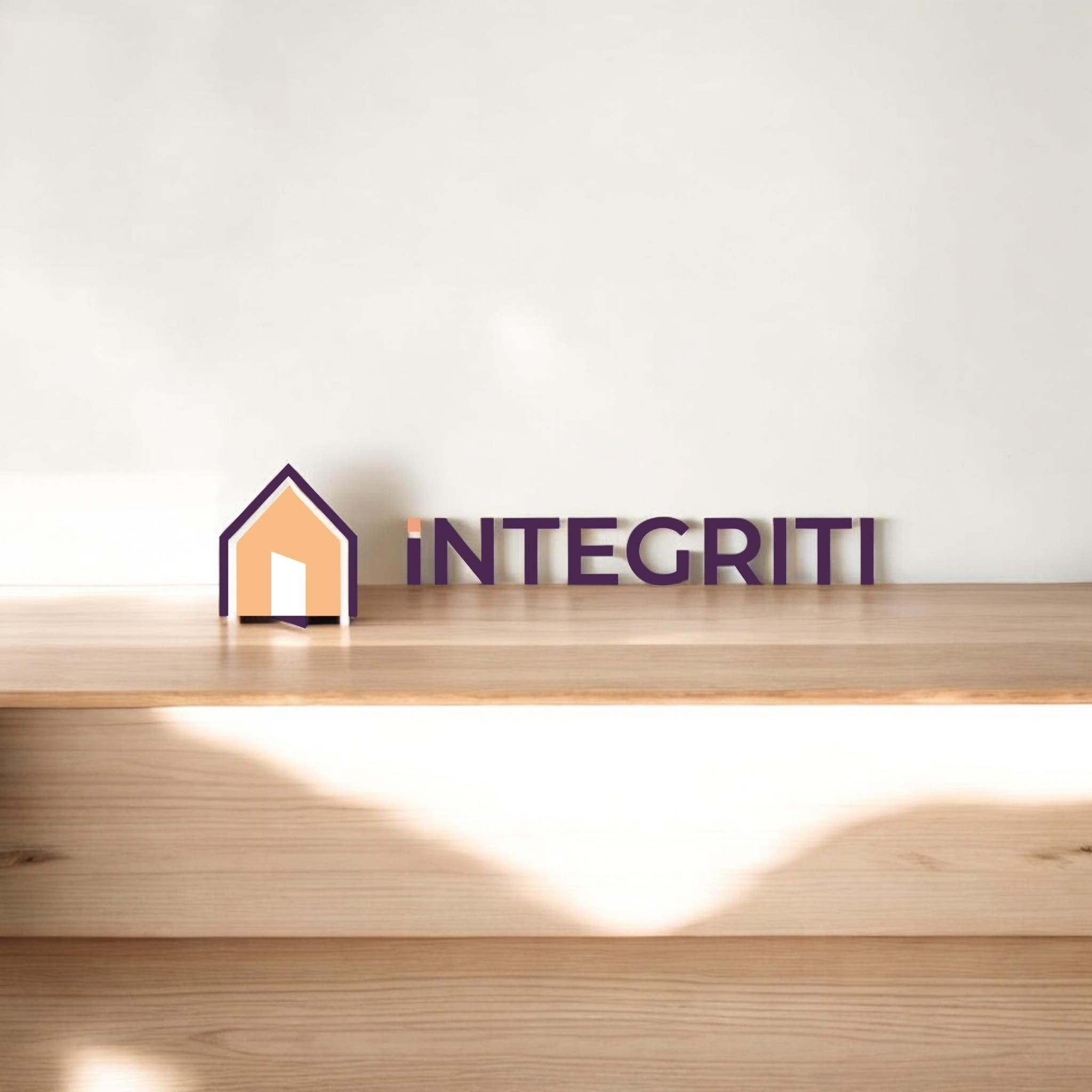 Drewniane logo firmy z napisem 'INTEGRITI' i symbolem domu w kolorach fioletu i beżu, umieszczone na drewnianej półce na tle białej ściany.