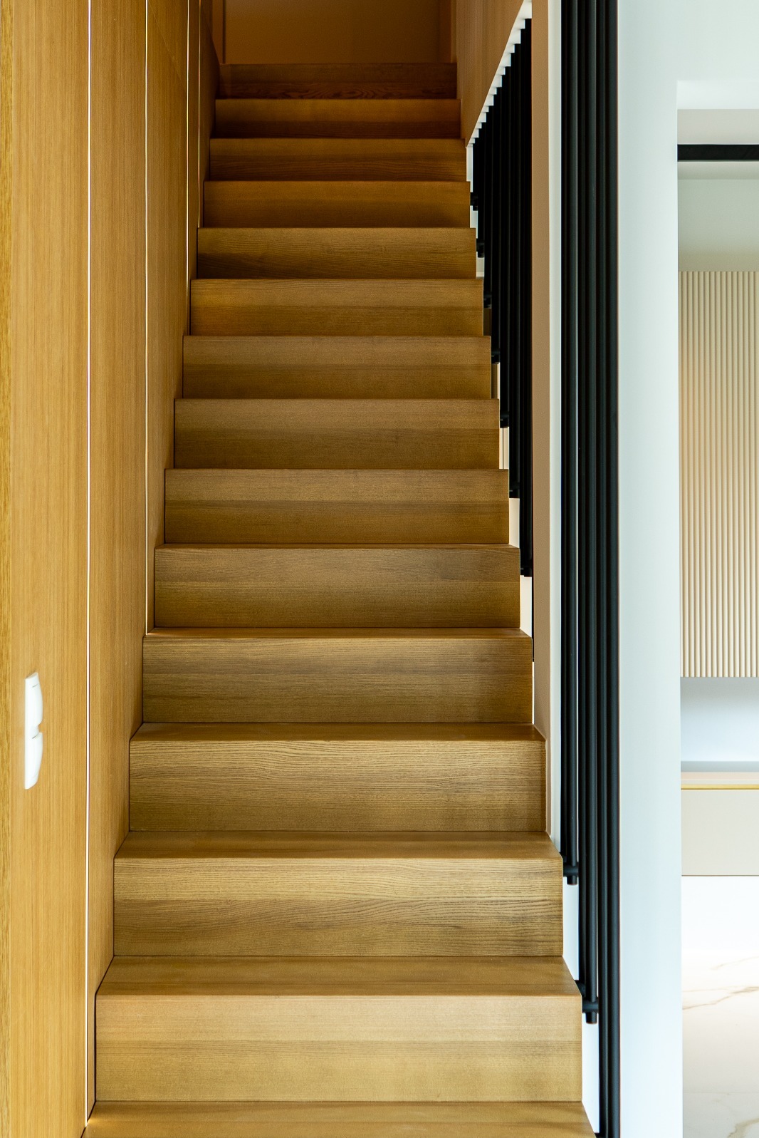 Drewniane schody z czarną balustradą w nowoczesnym wnętrzu w Warszawie. Naturalne oświetlenie podkreśla strukturę drewna.