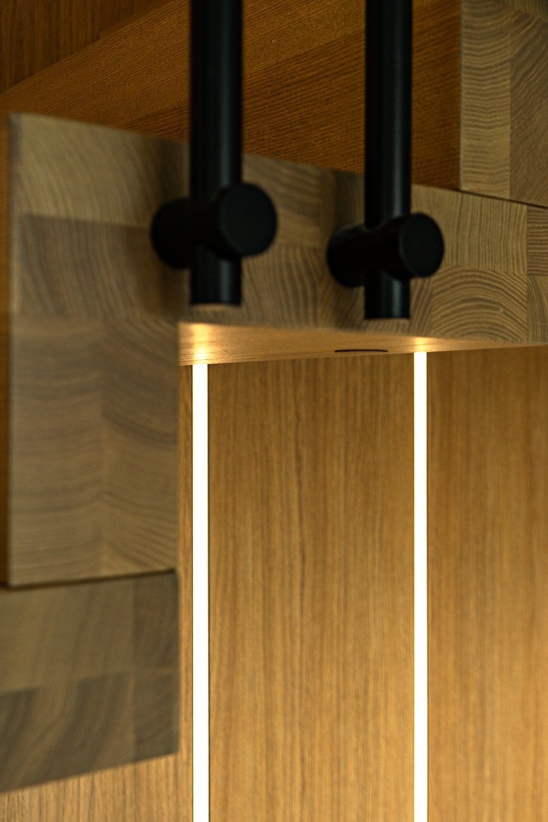 Drewniana zabudowa z oświetleniem LED i czarnymi lampami punktowymi. Widoczne detale struktury drewna i precyzyjny montaż oświetlenia.