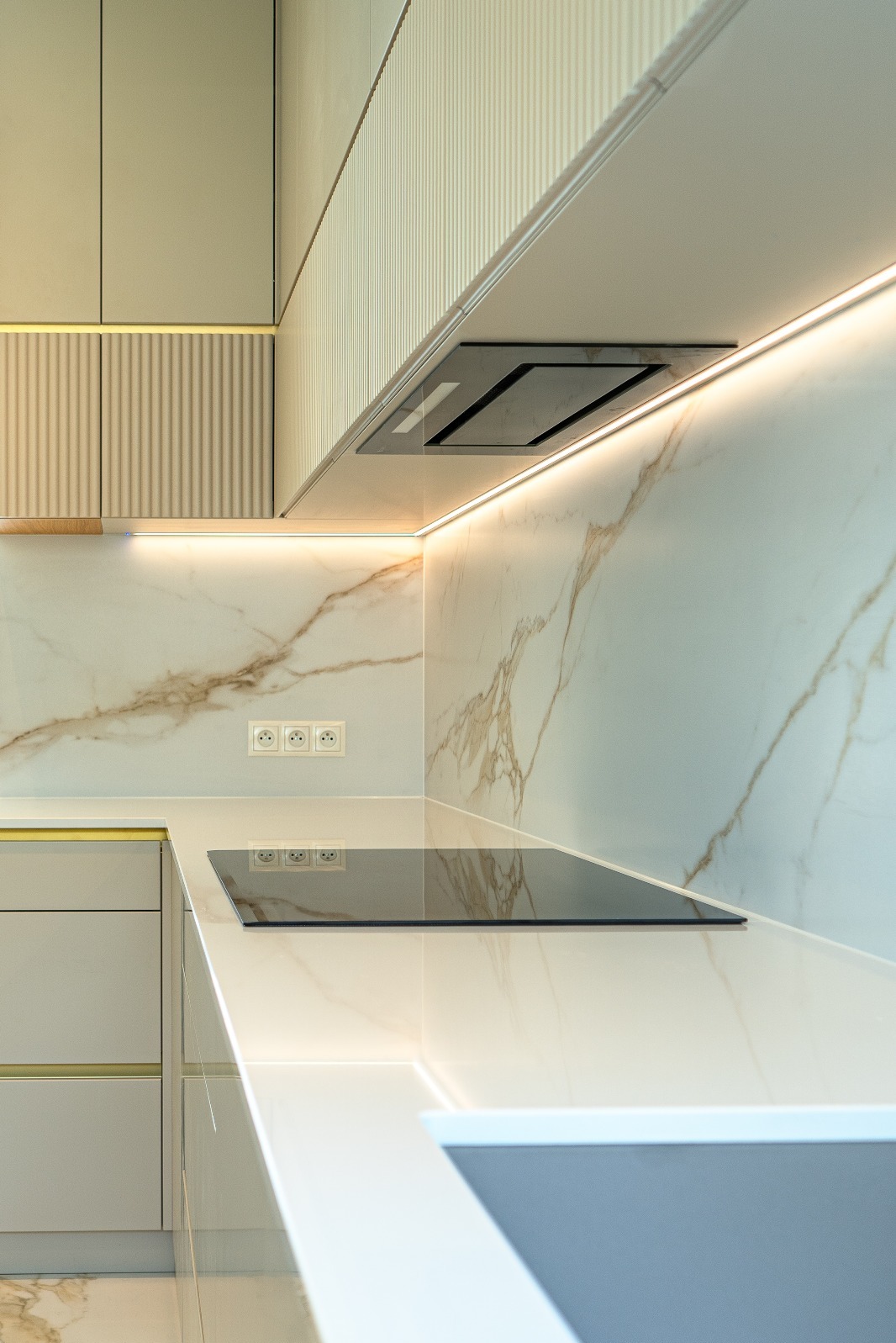 Nowoczesna kuchnia z marmurowym blatem i podświetleniem LED. Minimalistyczny design z płytą indukcyjną i eleganckim okapem. Widoczne gniazdka elektryczne.