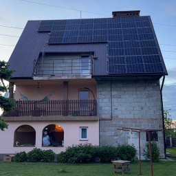 Nex Energy - Dom jednorodzinny z panelami słonecznymi na dachu, widocznymi od strony ogrodu, z balkonem i elementami konstrukcyjnymi z różnych materiałów.