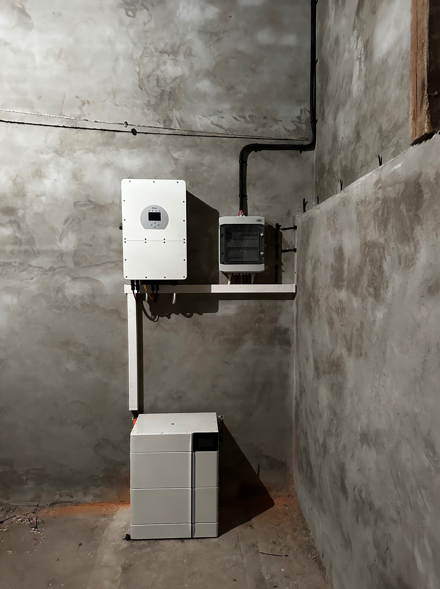 Biały inwerter, rozdzielnica elektryczna i moduł magazynu energii zamontowane na surowych, szarych ścianach wewnątrz budynku.