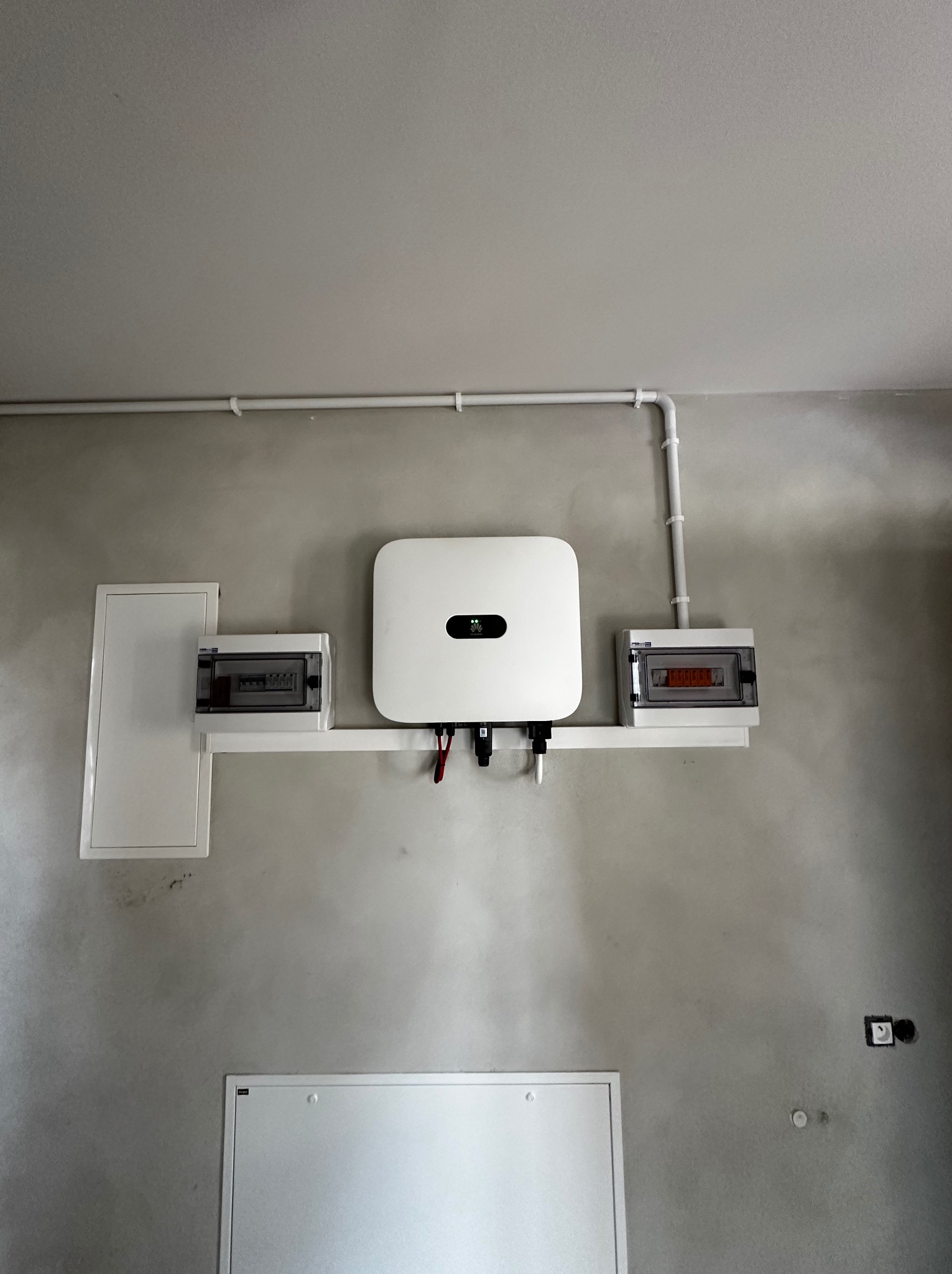 Biały inwerter fotowoltaiczny Huawei zamontowany na ścianie wewnątrz budynku, z widocznymi przewodami, zabezpieczeniami i instalacją elektryczną.