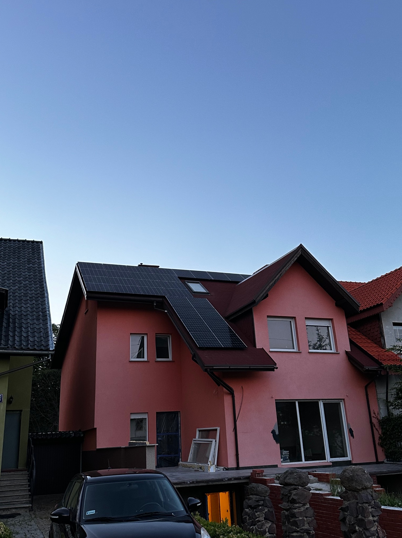 Różowy dom jednorodzinny z panelami słonecznymi na dachu, widok z dołu w pochmurny dzień.