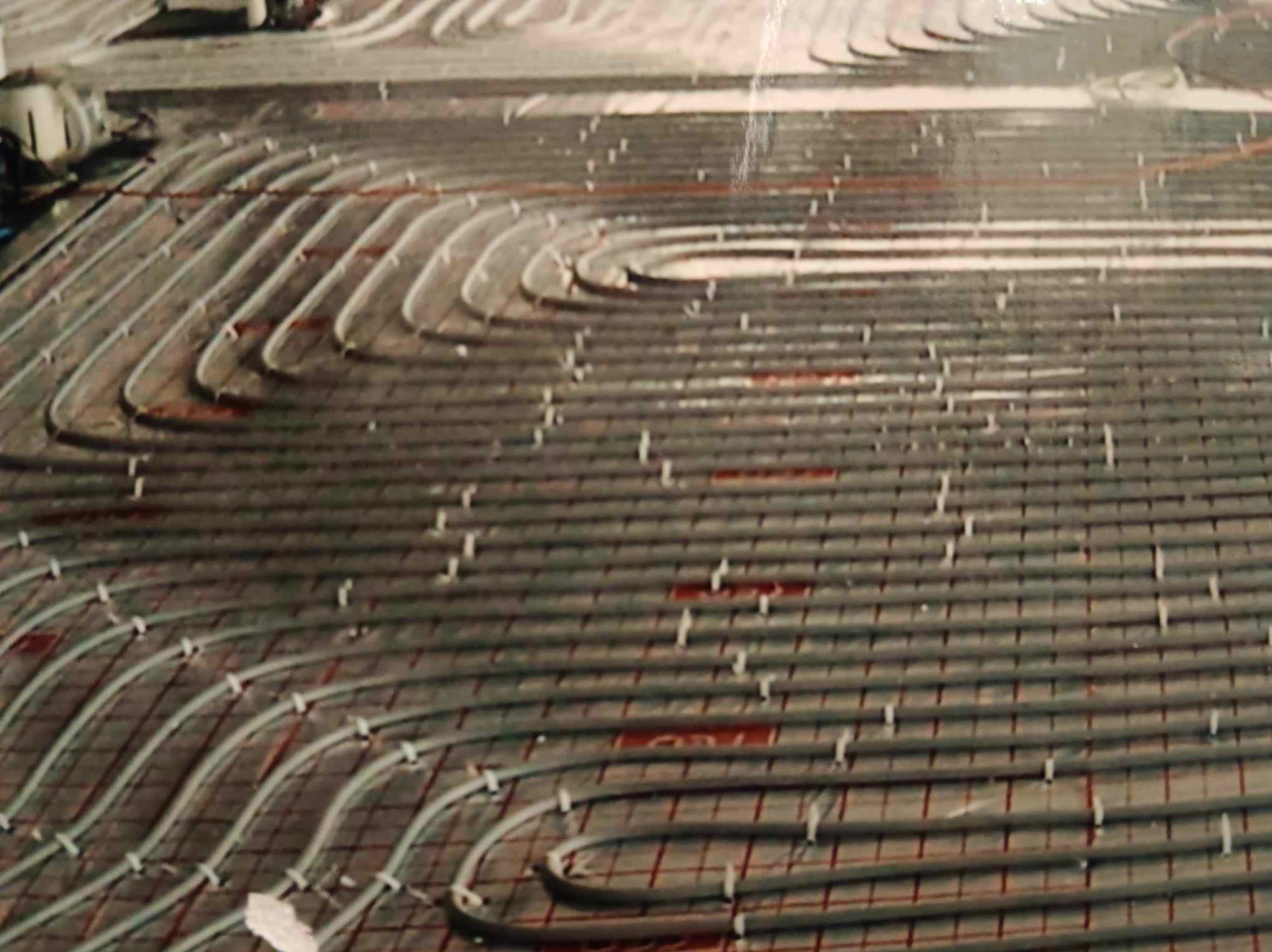 Układanie rur ogrzewania podłogowego na siatce z zaznaczonym rozstawem, widoczne mocowania rur do siatki, ujęcie z góry.