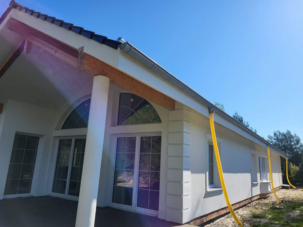 Biały dom jednorodzinny z nowoczesnymi oknami i żółtymi rurami spustowymi, widok z zewnątrz w słoneczny dzień.