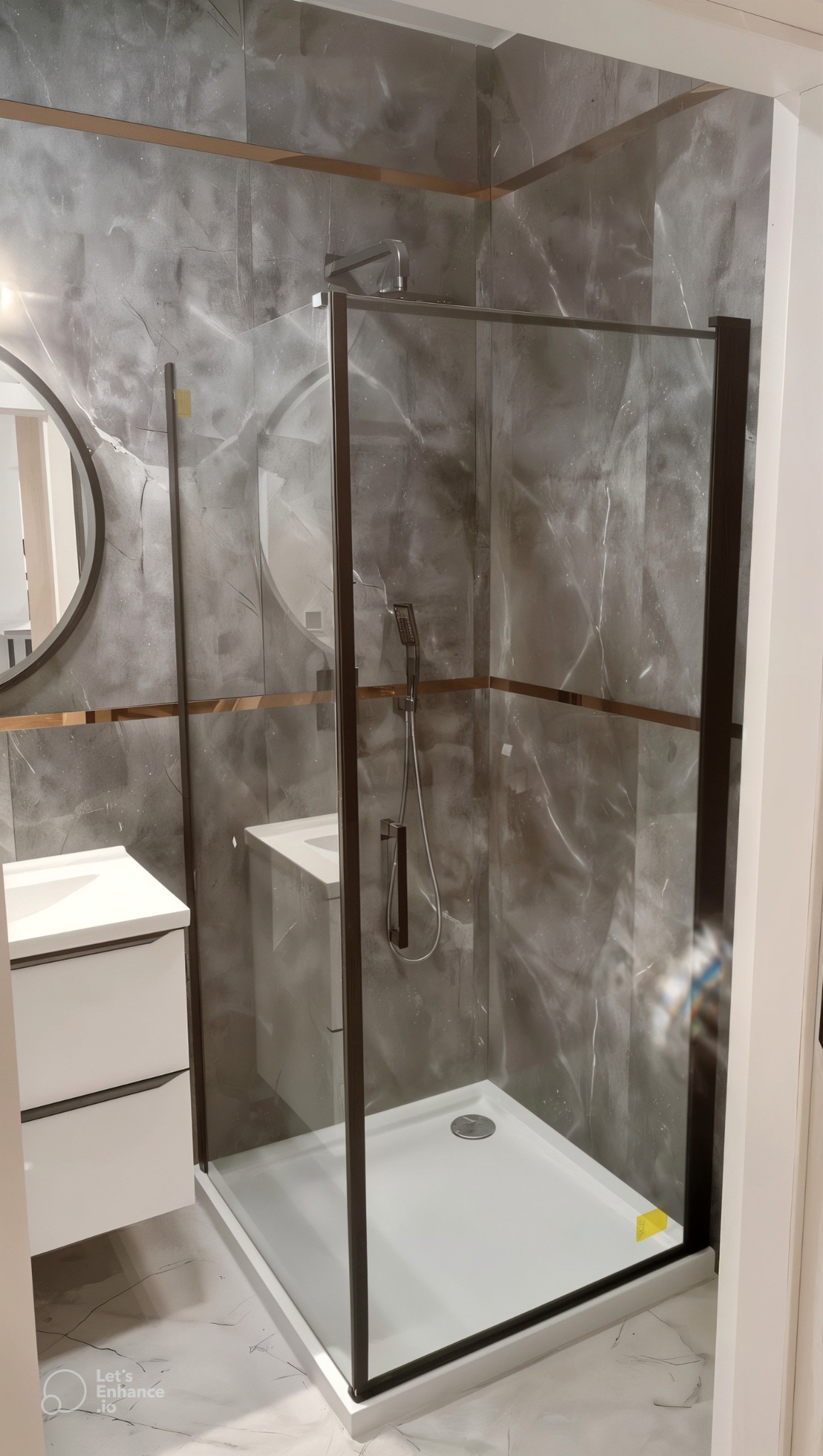 Nowoczesna kabina prysznicowa z czarnymi profilami, szare marmurowe płytki na ścianach, biała umywalka z szafką, okrągłe lustro z podświetleniem, złote listwy dekoracyjne.