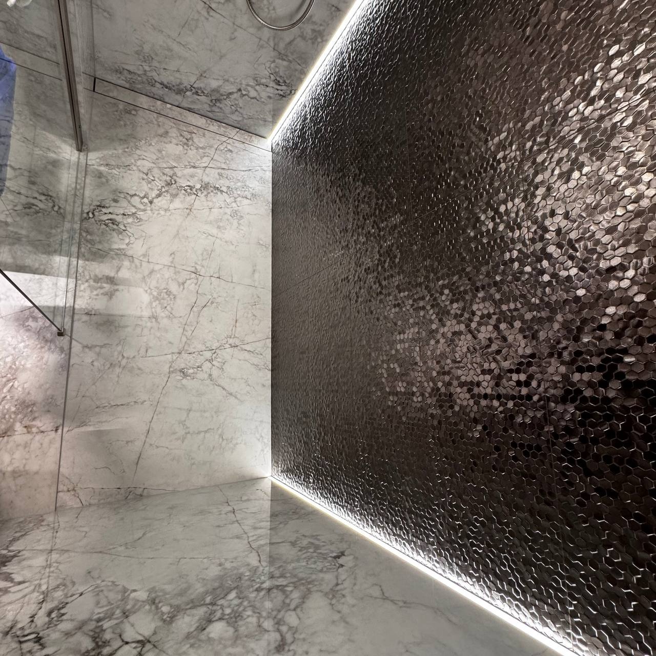 Nowoczesna łazienka z marmurowymi płytami i heksagonalną mozaiką, oświetlona listwą LED, tworząca elegancki i minimalistyczny design.