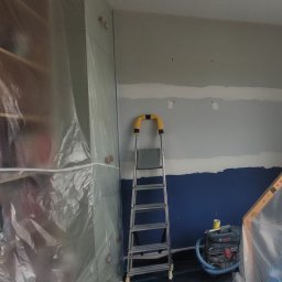 Zamalowywanie ściany pomalowanej w pasy o trzech rożnych kolorach, szpachlowanie łączeń pasów, żeby nie były widoczne po przemalowaniu na jeden kolor.