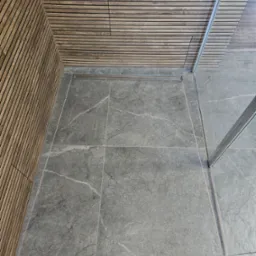 Szare płytki podłogowe w łazience z odpływem liniowym, drewniana okładzina ścienna z listewek i fragment szklanej kabiny prysznicowej.