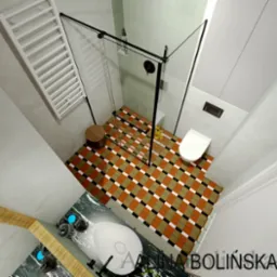 Wizualizacja łazienki z kabiną prysznicową z czarnymi ramami, umywalką na marmurowym blacie i podłogą w geometryczny wzór brązowo-biało-czarną szachownicę, widok z góry.