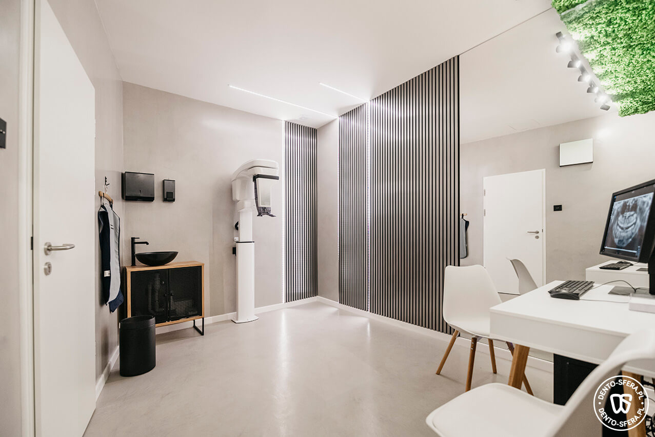 Wnętrze nowoczesnej kliniki stomatologicznej z aparaturą RTG, umywalką na szafce z metalową siatką, białymi krzesłami i ścianą z drewnianych listew.