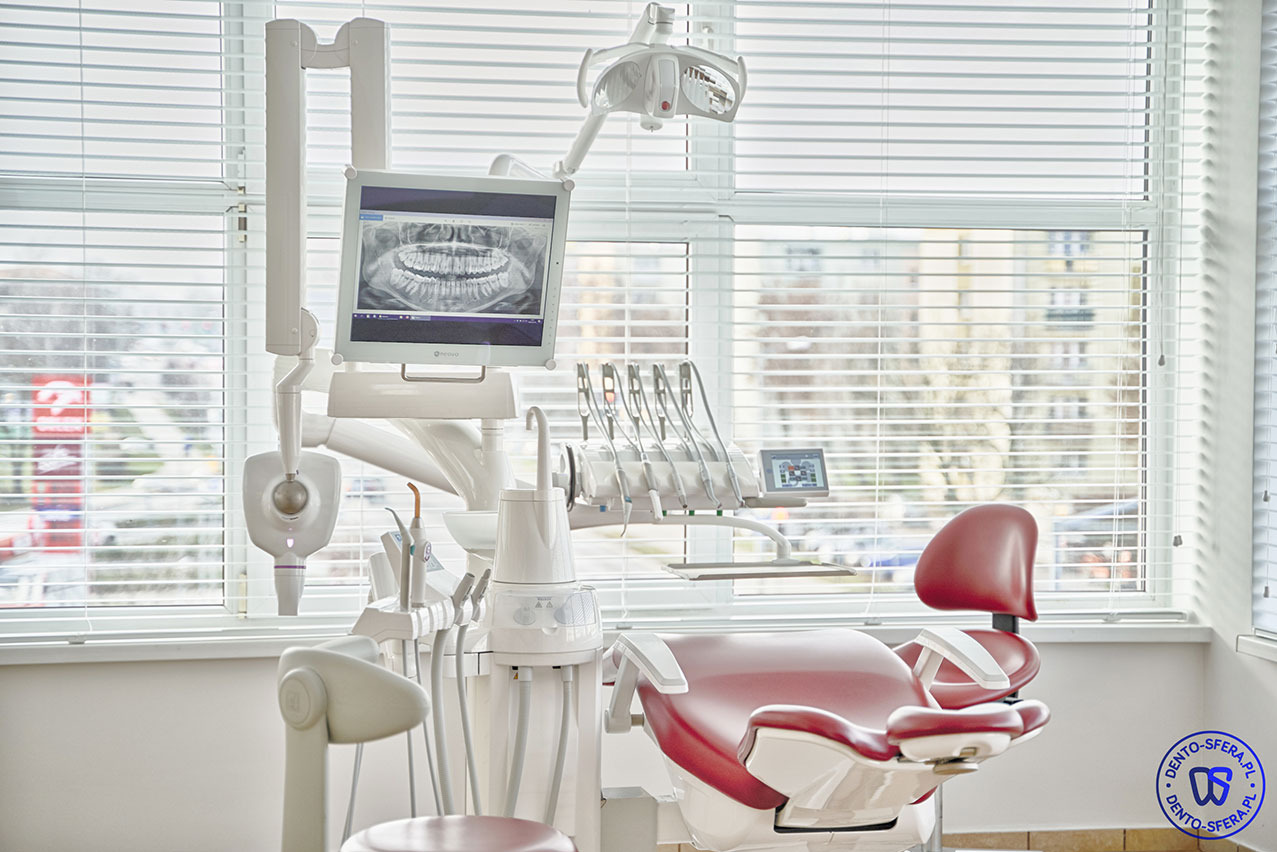 Nowoczesny gabinet dentystyczny z czerwonym fotelem, narzędziami i monitorem wyświetlającym zdjęcie rentgenowskie szczęki, oświetlony światłem dziennym wpadającym przez okno z żaluzjami.