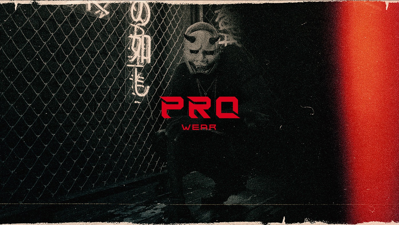 Mroczne ujęcie postaci w masce demona za siatką z logo 'PRO WEAR' nałożonym cyfrowo, z efektem ziarna i czerwonym paskiem po prawej stronie.