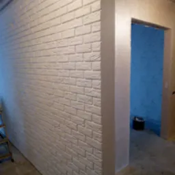 Ściana pokryta dekoracyjną, białą cegłą z widocznym wejściem do pomieszczenia z niebieską ścianą, ujęcie z boku.