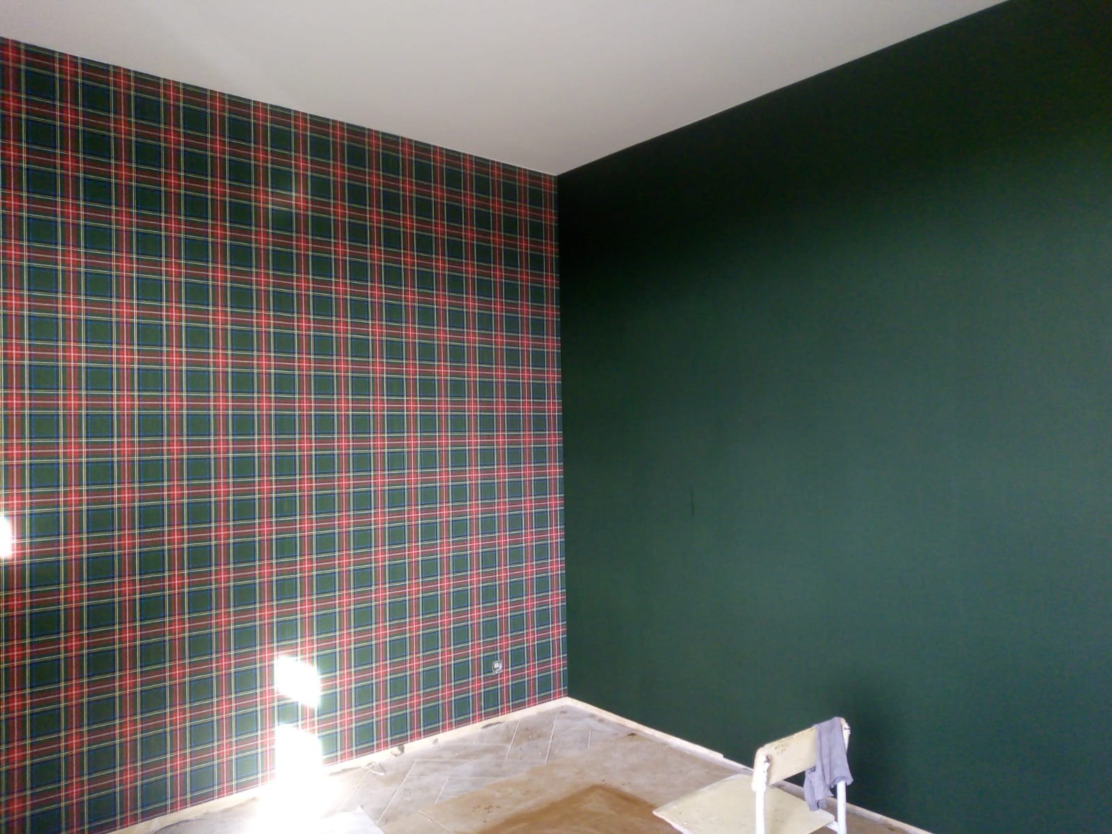 Pokój po odnowieniu: jedna ściana w kratę szkocką, druga pomalowana na ciemnozielono, widoczny fragment podłogi i krzesło z szarą szmatką.