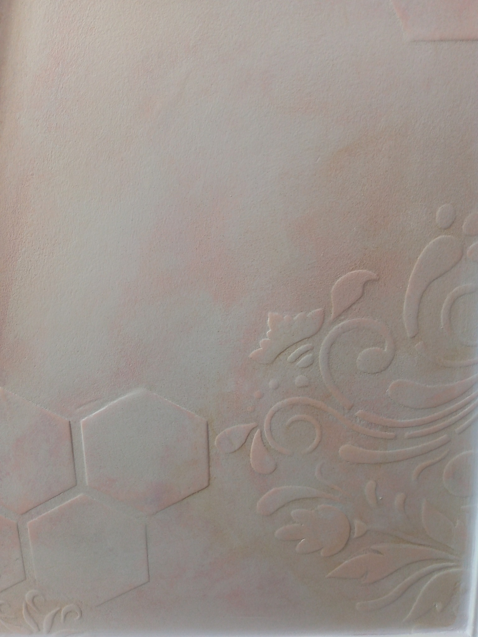 Jasnoróżowa ściana z dekoracyjnym wzorem kwiatowym i geometrycznym, wykonana techniką strukturalną, prezentująca efektowną fakturę.