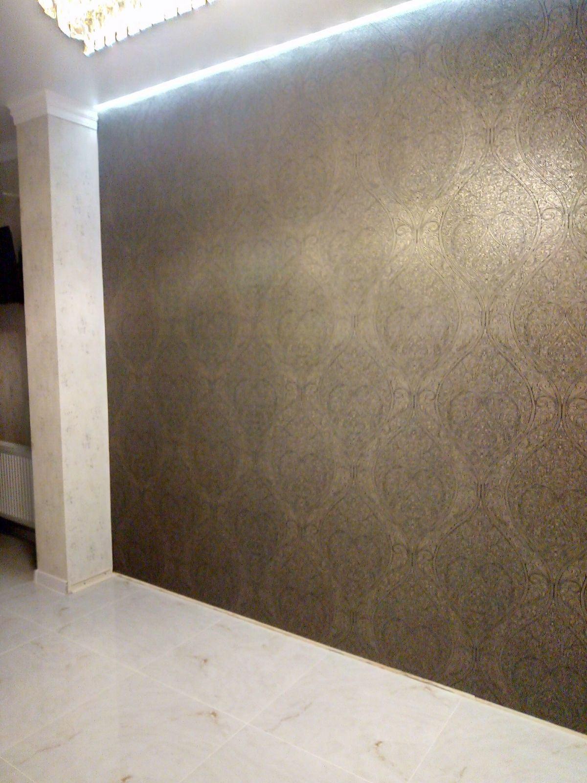 Elegancka ściana z dekoracyjną fakturą w odcieniach brązu, oświetlona ledowym światłem, widok z dołu, jasna podłoga i fragment kolumny w rogu.