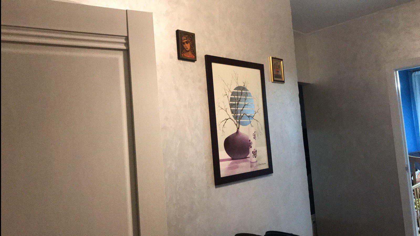 Ściana z efektem dekoracyjnym, na której wiszą obrazy w ramkach. Widoczny fragment drzwi i przejście do innego pomieszczenia.