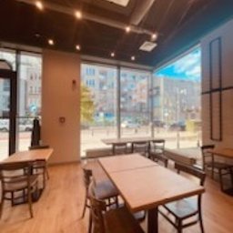 Remonty I wykonczenia - Jasne, przestronne wnętrze biurowe po malowaniu, widoczne drewniane podłogi, stoliki i krzesła, duże okna z widokiem na miasto, białe ściany z szarymi akcentami, sufit z oświetleniem punktowym...